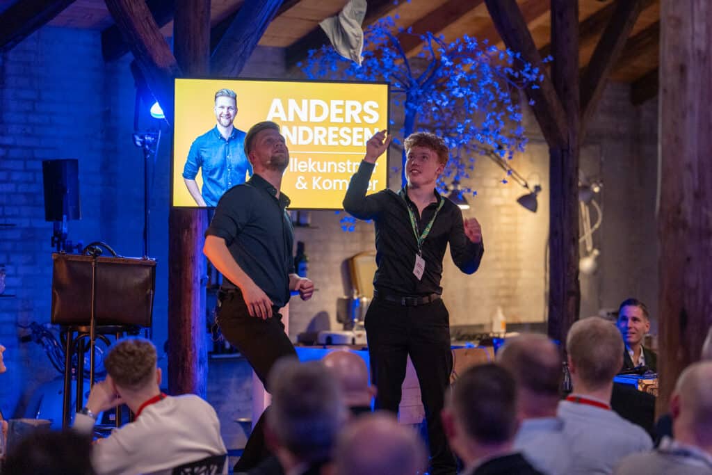 Gæst og Anders Andresen med armene i vejret foran et livligt publikum